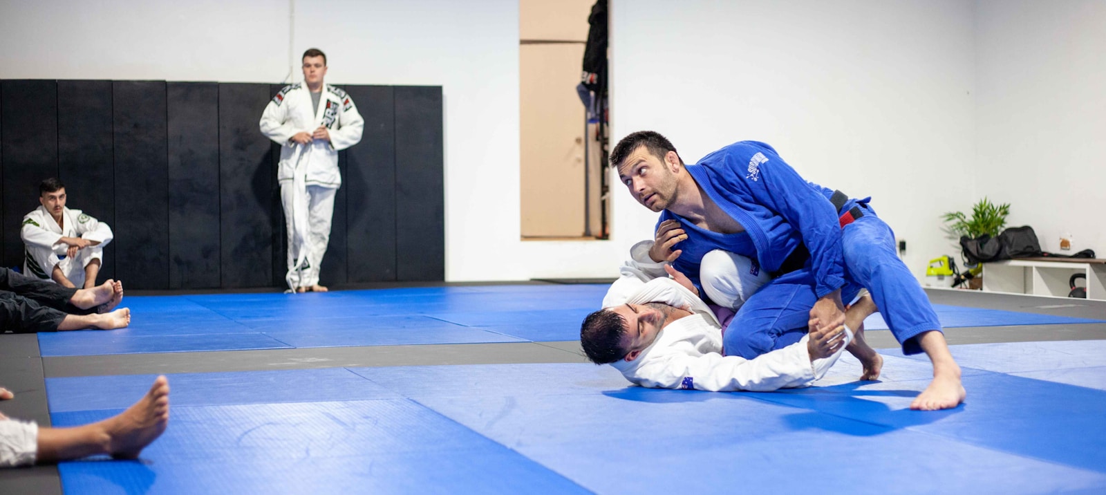 Two people practicing grappling on mats in a martial arts gym