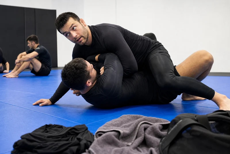 Two people practicing grappling on mats in a martial arts gym